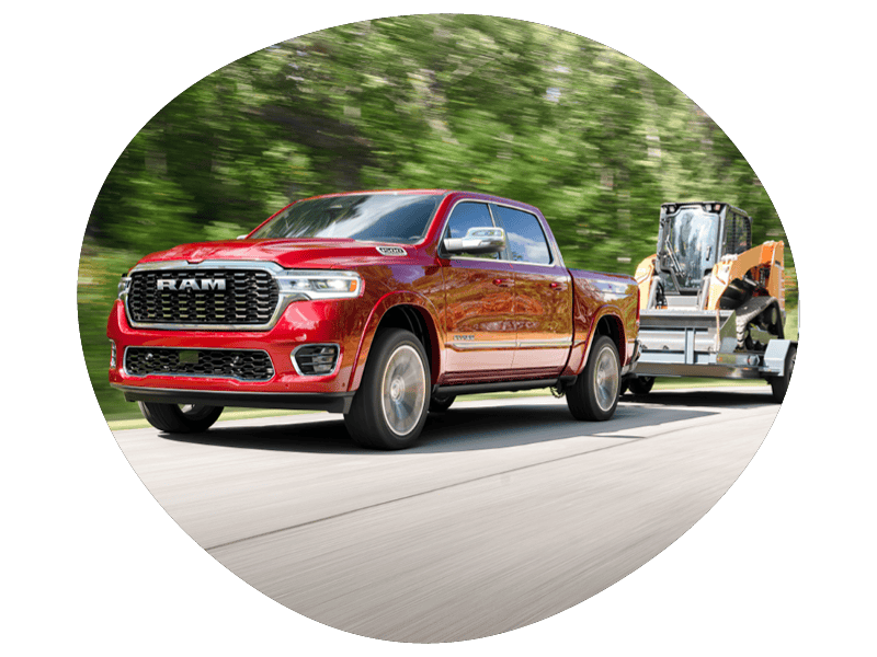 Red RAM pickup truck towing construction equipment on trailer along a forested road, motion blur background, showcasing towing capability, power, and heavy-duty performance.