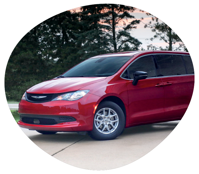 Red Chrysler minivan parked on a driveway with trees and a sunset sky in the background.